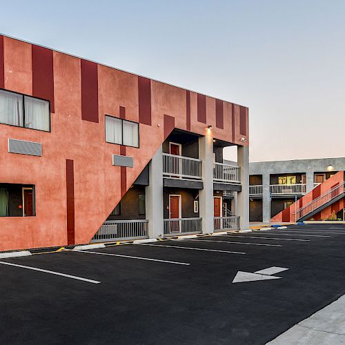 A modern building with a colorful geometric facade and an empty parking lot in front is shown in the image.