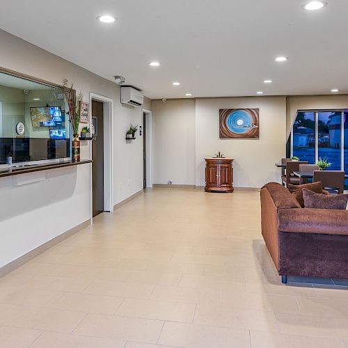 A modern, well-lit waiting room with a reception desk, brown couches, small tables and chairs, decor items, and large windows.