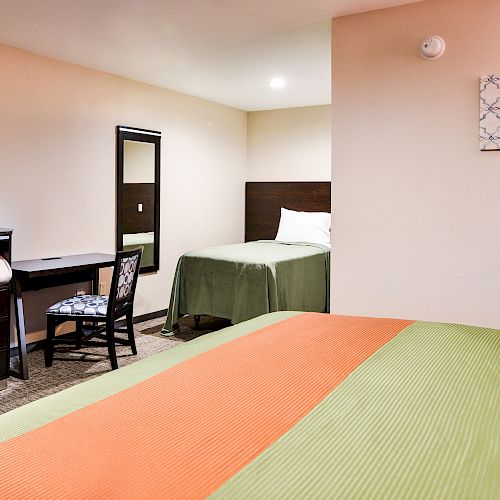 The image shows a hotel room with two beds, a flat-screen TV, a desk and chair, a mini-fridge, and a piece of wall art.