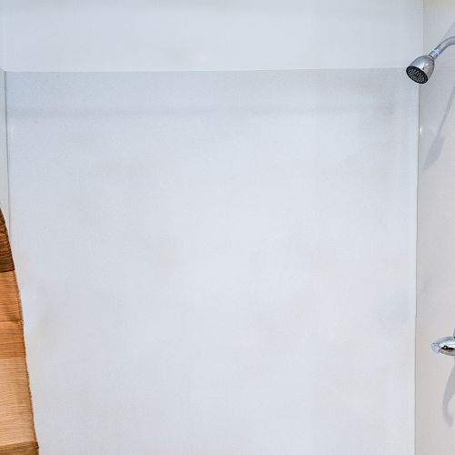 The image shows a simple shower area with a showerhead on the upper right and a faucet handle below it, with a brown and beige shower curtain.