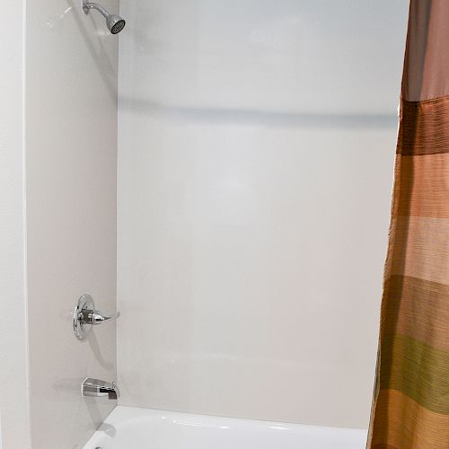 The image shows a clean, white bathtub and shower with a colorful striped curtain partially drawn to the side.