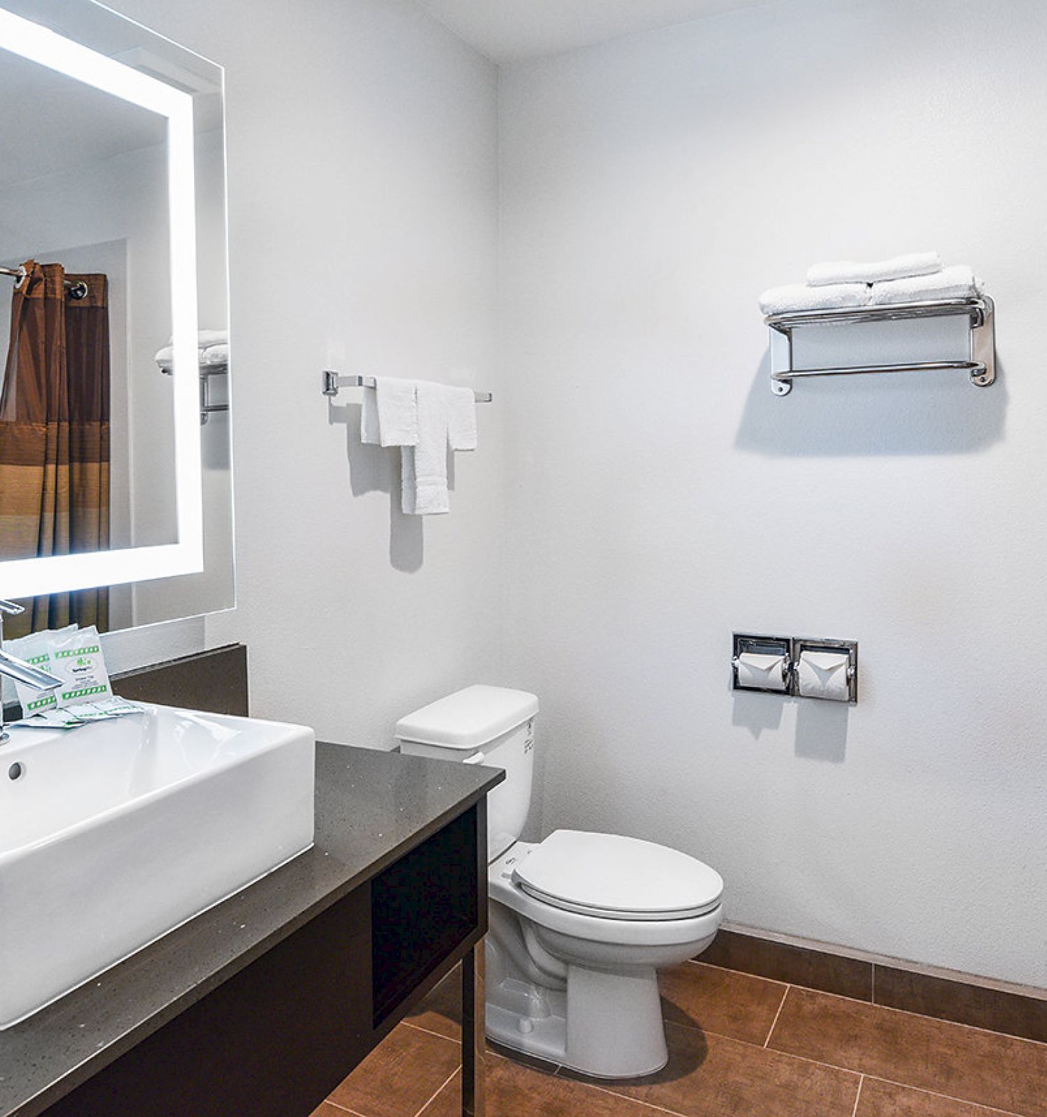 A clean bathroom featuring a sink with a mirror, a toilet, and towels on a shelf and rack.