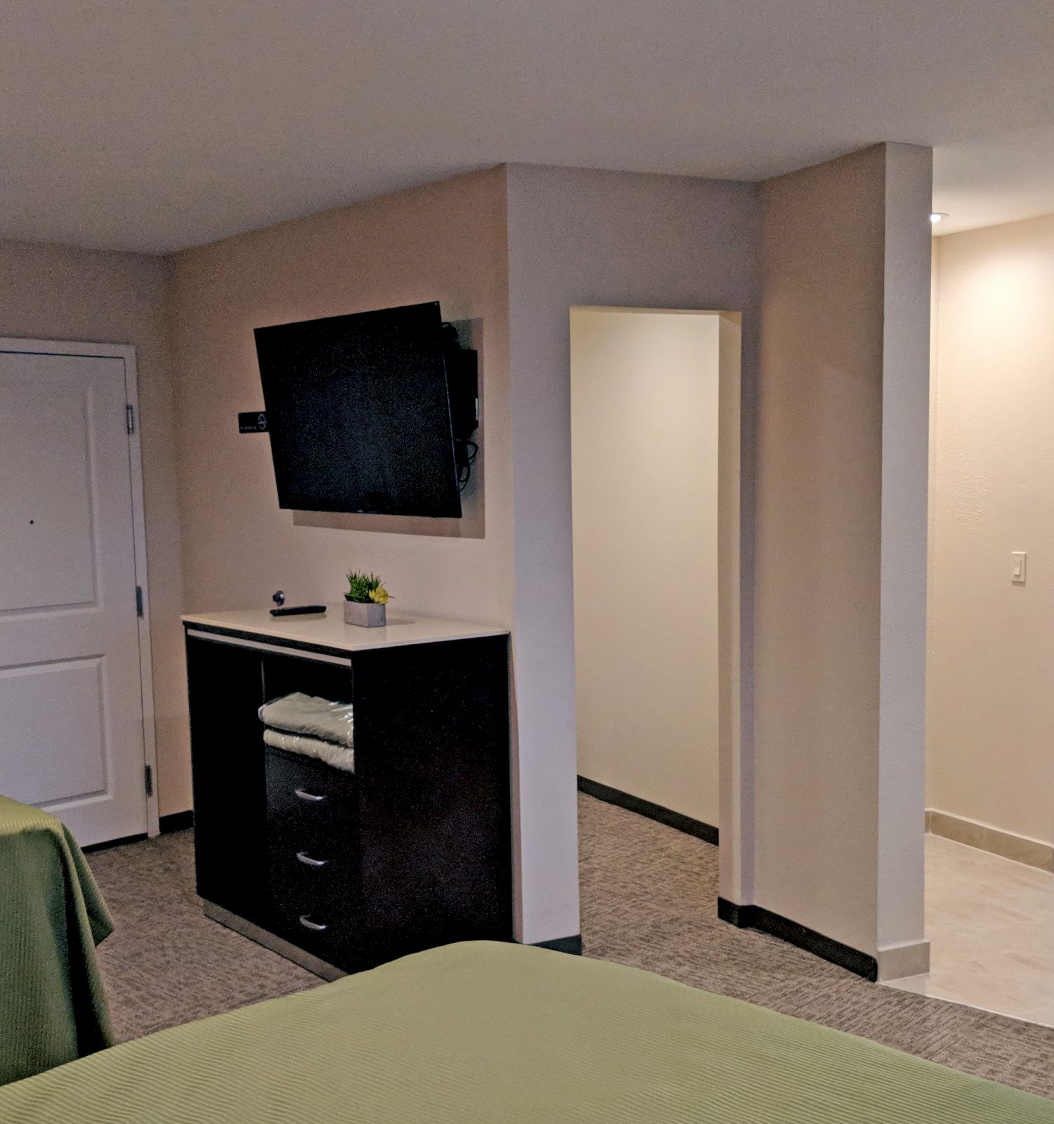 The image shows a hotel room with two beds, a wall-mounted TV, a doorway leading to a bathroom, and some furniture. The room has a modern design.