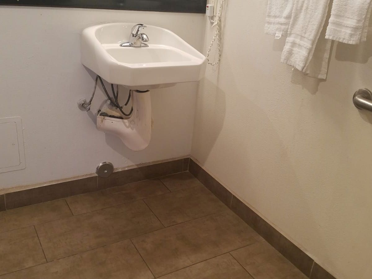 A bathroom with a wall-mounted sink, towels on a rack, a grab bar, and a toilet paper holder on the side.