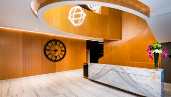 A modern lobby with a curved wooden ceiling, marble counter, large clock on the wall, and floral arrangement on the counter.