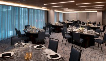 The image shows an elegantly set dining area with round tables, black chairs, and decorative centerpieces, likely prepared for an event or banquet.