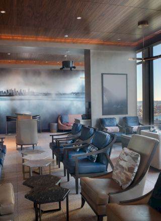 A modern lounge area with plush seating, a wall mural, large windows offering a scenic view of a coastline, and a ferris wheel visible outside.