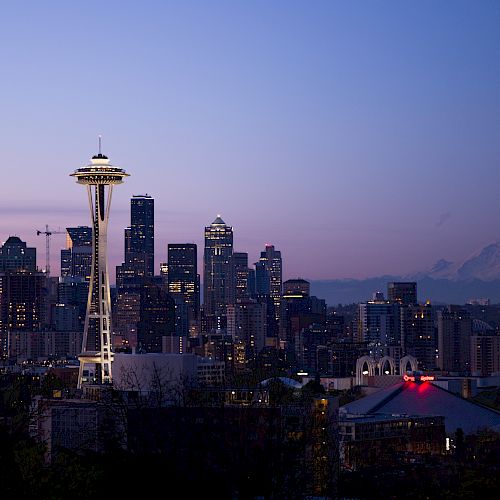 City skyline at dusk with the iconic Space Needle prominently visible; Mount Rainier stands in the background, adding to the scenic beauty.